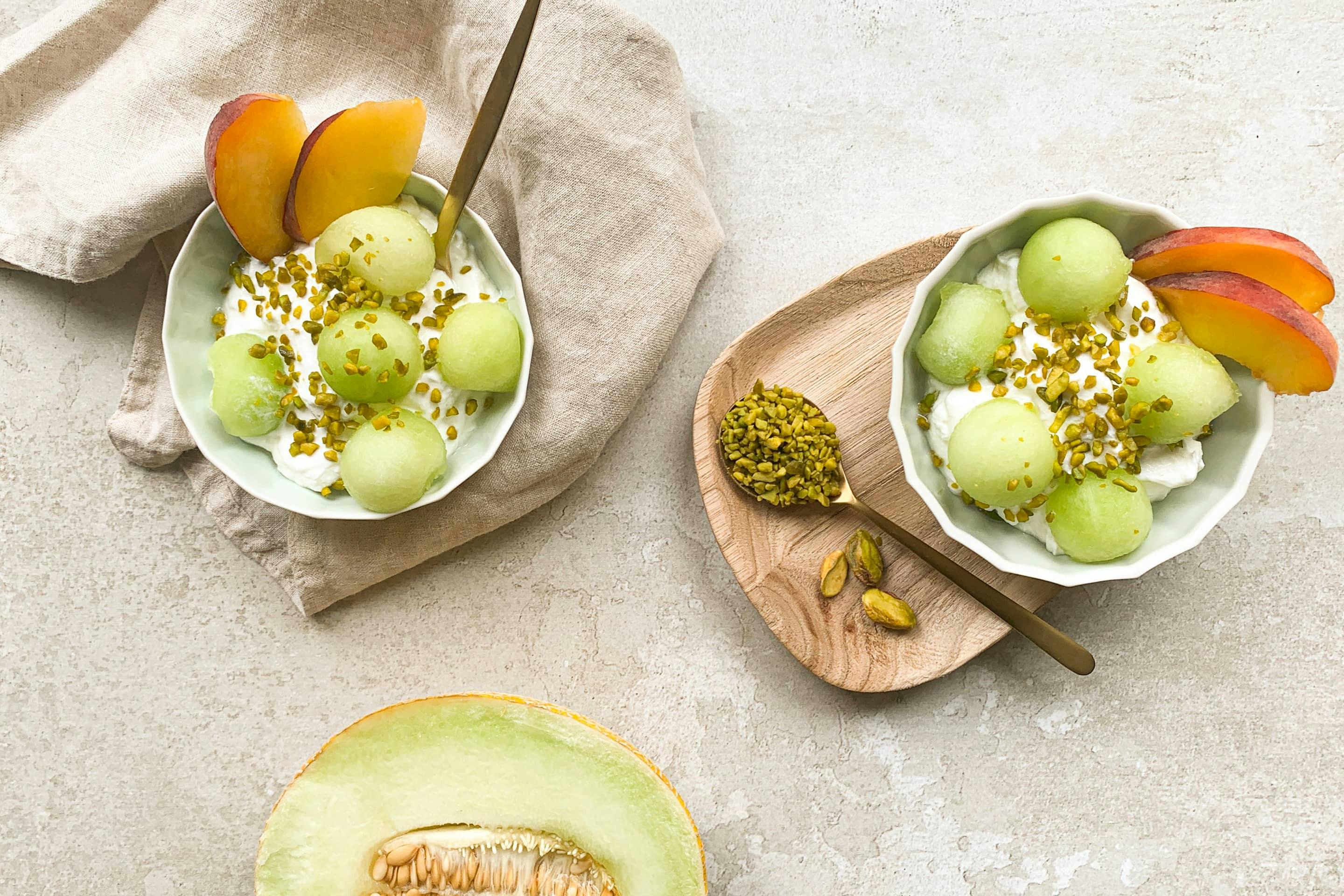 2 posodici melonininega jogurta obloženga z melono, breskvijo in posutega s pistacijo