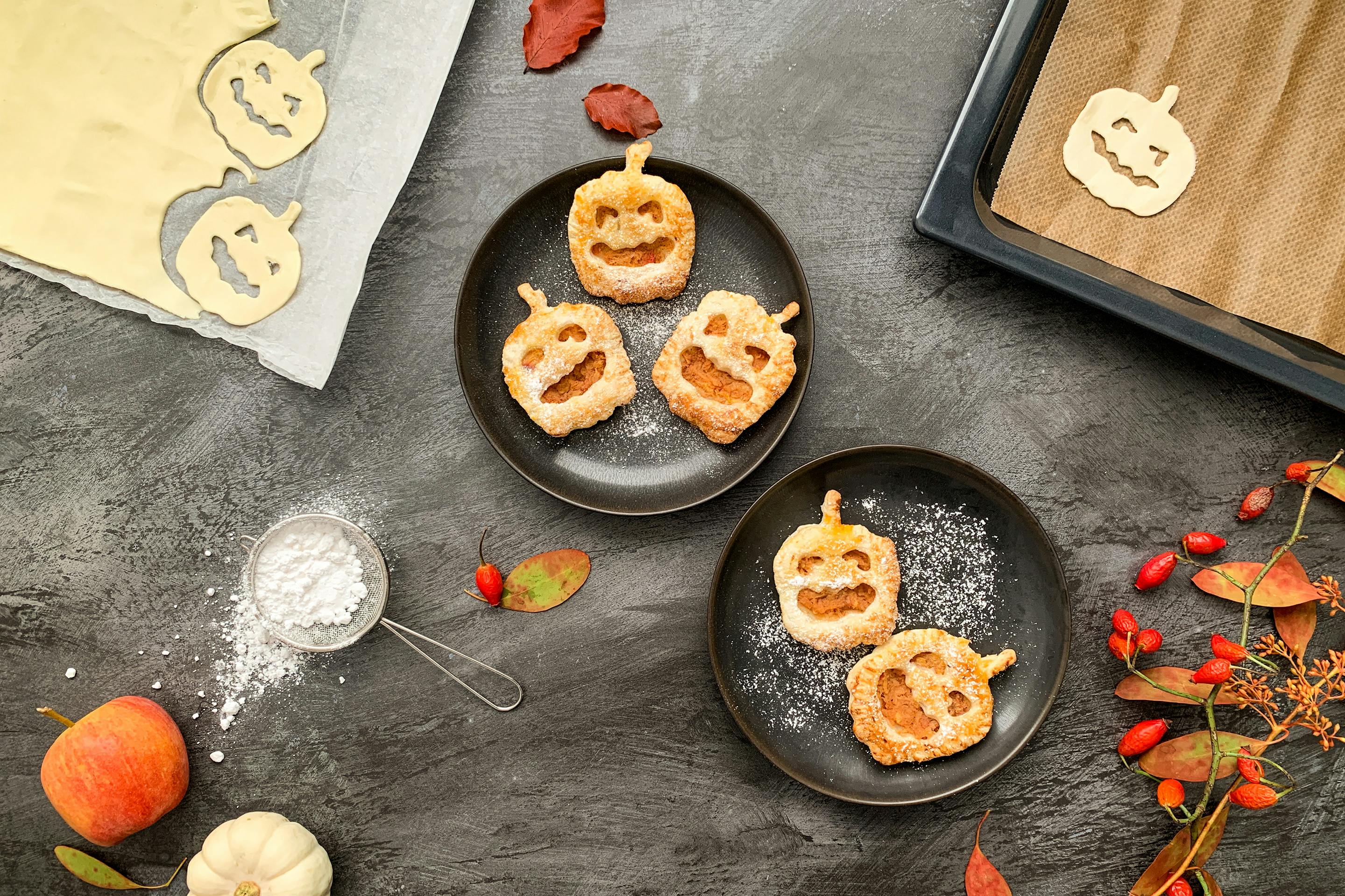 Jabolčni zavitki v obliki buč primerni za Halloween servirani na krožnikih zraven listnatega testa